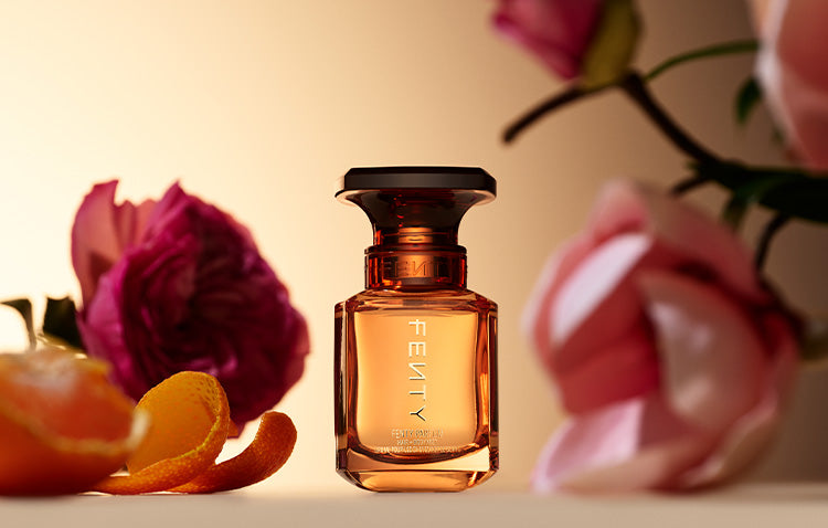Fenty Parfum Hiar + Body Mist against a background with flowers and citrus.