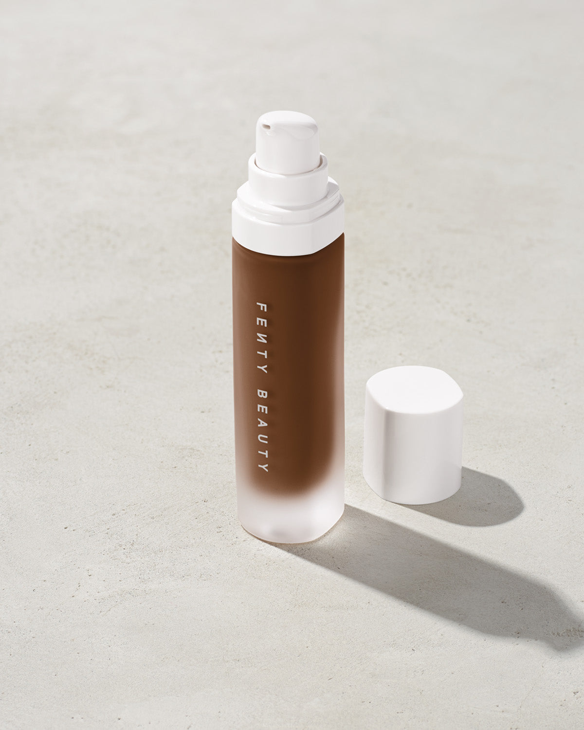 open bottle of Fenty Beauty Pro Filt'r Soft Matte Longwear Foundation with pump dispenser in shade 490 on concrete background